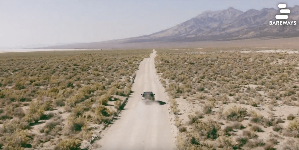 Eine Bildschirmaufnahme aus eine Video von Bareways. Ein Auto fährt durch eine ausgetrocknete Landschaft, weg von der Kamera.